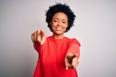 Kıvırcık saçlı, kırmızı kazaklı, genç, Afro-Amerikan bir kadın. Seni ve kamerayı işaret ediyor.
