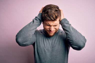 Sakallı, mavi gözlü, başağrısı yüzünden acı çeken, çaresiz ve stresli bir süveter giyen genç yakışıklı sarışın adam. Ellerini başının üstüne koy..