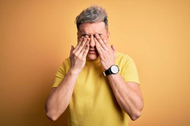 Sarı izole edilmiş arka plan üzerine sarı tişört giyen yakışıklı modern bir adam yorgunluk ve baş ağrısı için gözlerini ovuşturuyor, uykulu ve yorgun bir ifade takınıyor. Görüş sorunu