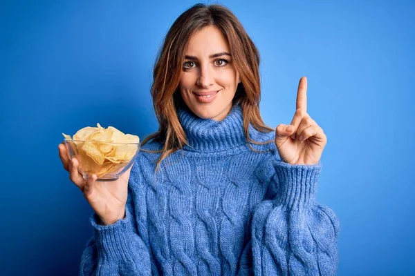 Young Beautiful Brunette Woman Holding Bowl Potato Chips Blue Background — Stock Photo, Image