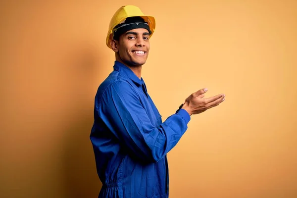 年轻英俊的非洲裔美国人 身穿蓝色制服 头戴安全帽 双手张开手掌 展示复制空间 呈现广告笑容 喜形于色 — 图库照片