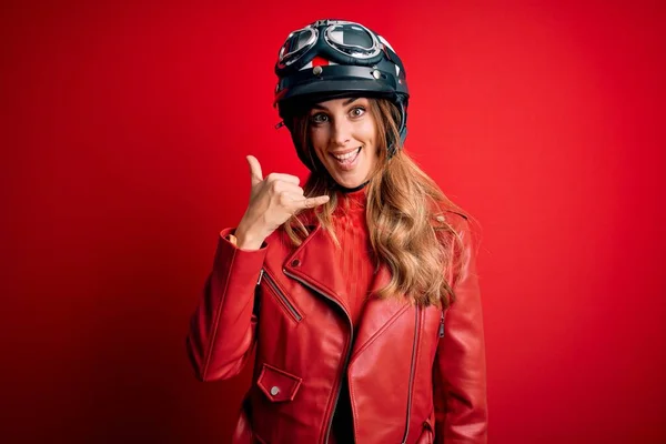 赤い背景の上に元ヘルメットを身に着けている若い美しいブルネットのオートバイの女性は 電話で話すような手と指で電話のジェスチャーをして笑っています 概念の伝達 — ストック写真
