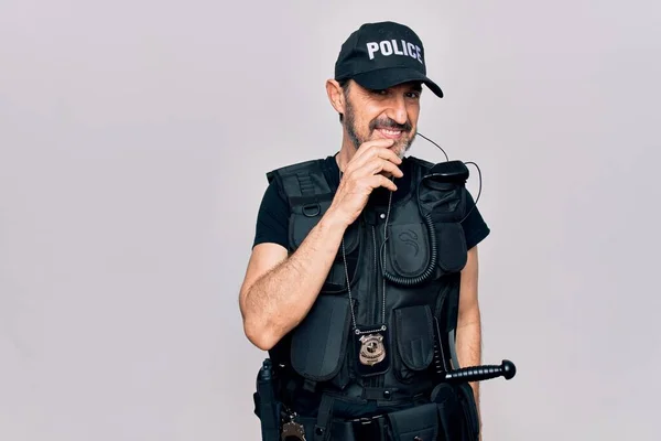 警察の制服と防弾チョッキを着た中年警官が白い背景に笑みを浮かべてカメラを見て自信を持って顔を交差腕と顎の手 肯定的な考え — ストック写真