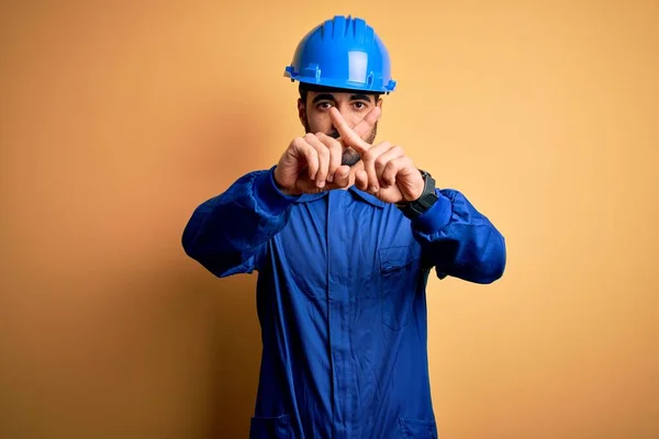 黄色の背景に青い制服と安全ヘルメットを身に着けているひげを持つ機械的な男否定的な記号を行う指を横断拒否式 — ストック写真