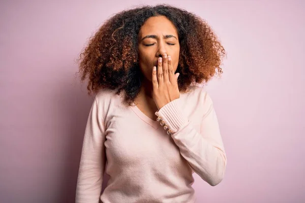 ピンクの背景にカジュアルなセーターを着てアフロの髪を持つ若いアフリカ系アメリカ人女性は 手で口をカバー疲れあくび退屈 眠れないのか — ストック写真