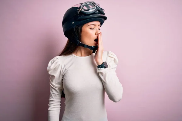 ピンクの背景に元ヘルメットをかぶって青い目をした若い美しいオートバイの女性は 手で口をカバー疲れYawning退屈 眠れないのか — ストック写真