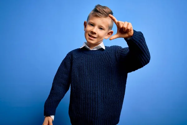 青い背景に冬のセーターを着た青い目の若い白人の子供は笑顔で 指を見てカメラで小さなサイズの看板をして手で自信を持ってジェスチャー 概念の測定 — ストック写真