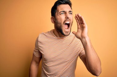 Sarı arka planda sıradan çizgili tişörtler giyen sakallı yakışıklı genç adam el ele tutuşarak bağırıyor ve bağırıyordu. İletişim konsepti.