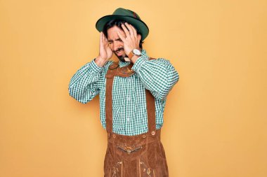 Almanya festivali için geleneksel Alman Ekim Festivali kıyafeti giyen yakışıklı genç bir adam acı ve migrenden dolayı çaresiz ve stresli bir baş ağrısı çekiyor. Ellerini başının üstüne koy..