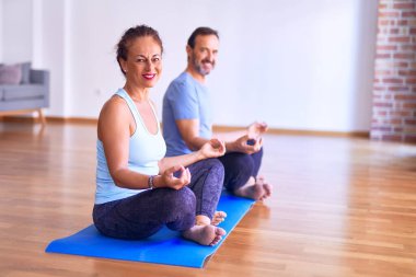 Orta yaşlı güzel sporcu çift mutlu gülümsüyor. Paspasın üzerinde oturup yoga çalışmak spor salonunda nilüfer pozu vermek.
