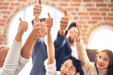 Bir grup iş adamı mutlu gülümsüyor. Ofiste baş parmaklarınla dikiliyorsun.