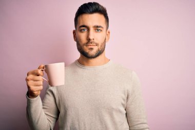 Genç yakışıklı bir adam pembe izole edilmiş arka planda bir fincan sıcak kahve içiyor. Zeki bir yüz ifadesiyle ciddi ciddi düşünüyor.