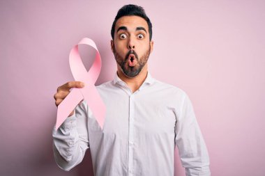 Sakallı, pembe kanser kurdelesi takan genç yakışıklı bir adam. Şok geçirmiş, şaşırmış ve korku ifadesinden korkmuş.