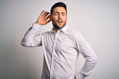 Zarif bir gömlek giyen yakışıklı bir adam izole edilmiş beyaz arka plan üzerinde duruyor yorgun ve rahat, uykulu ve sabahın erken saatleri için esniyor.