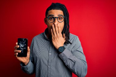 Genç Afrikalı Afro-Amerikan bir adam elinde kırık bir akıllı telefon tutarken ekranın çatırdayan ağzını gösteriyor. Utanç verici bir hata, korku ifadesi, sessizlikten korkmak, gizli bir konsept.