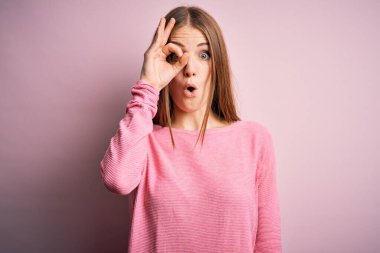 Genç, güzel, kızıl saçlı bir kadın pembe arka planda rahat bir süveter giyiyor. Şaşırmış yüz ifadesiyle, parmaklarından bakan gözleriyle şaşırmış bir jest yapıyor. İnançsız ifade.