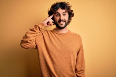 Sakallı, sıradan bir süveter giyen, sarı arka planda duran yakışıklı genç bir adam. Bir parmağıyla gülümseyerek, harika bir fikir ya da düşünceyle, iyi bir hafızayla.