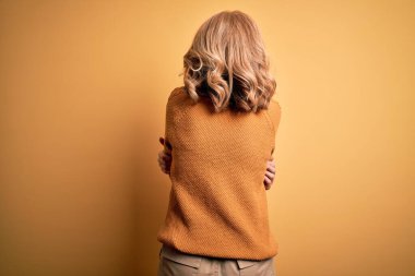 Sarışın, orta yaşlı, sıradan bir süveter ve sarı arka planda gözlük takan güzel bir kadın mutlu ve pozitif bir şekilde sarılıyor. Sevgi ve özgüven.