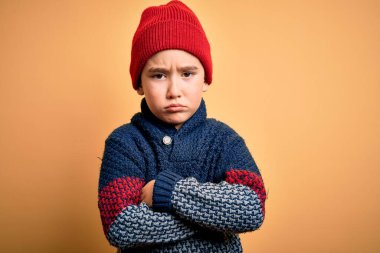 Sarı izole edilmiş arka planda yünlü kazak giyen küçük bir çocuk şüpheci ve gergin, yüzünde çapraz kollu tasvip etmeyen bir ifade. Negatif kişi.