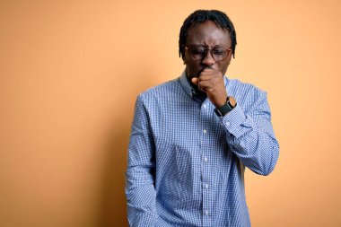 Sarı arka planda gömlek ve gözlük takan yakışıklı Afro-Amerikan erkeği kendini iyi hissetmiyor ve soğuk algınlığı veya bronşitin belirtisi olarak öksürüyor. Sağlık hizmeti kavramı.