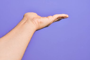 İzole edilmiş mor arka plan üzerinde parmaklarını gösteren beyaz bir gencin eli. Düz avuç içi ürünü sunuyor, el hareketi yapıyor, boş kopya alanı veriyor.
