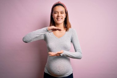 Genç, güzel bir kız hamile, pembe arka planda bebek bekliyor. Ellerinde büyük ve büyük bir işaret var. Ölçüm sembolü. Kameraya bakıp gülümsüyor. Ölçüm konsepti.