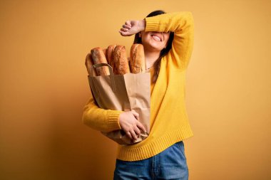 Sarı arka planda bir torba taze sağlıklı ekmek tutan genç ve güzel bir kadın. Gülümseyen, güler yüzlü, elleri açık bir şekilde dikizleme oyunu oynayan. Şaşırdım ve çıktım.