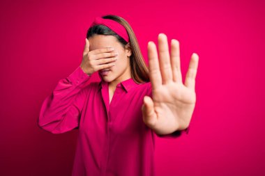 Genç ve güzel esmer kız, günlük gömleğini giymiş, pembe arka planda dikiliyor, gözleri ellerle kaplıyor ve üzgün ve korku ifadeleriyle jest yapıyor. Utanç verici ve olumsuz bir kavram..