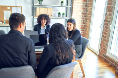 Bir grup iş adamı mutlu ve kendinden emin gülümsüyor. Yüzünde gülümsemeyle çalışmak, dizüstü bilgisayar kullanmak ve ofiste konuşmak.