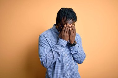 Sarı arka plan üzerine gömlek ve gözlük takan yakışıklı Afro-Amerikan bir adam. Ağlarken yüzünü ellerle kapatan üzgün bir ifade. Depresyon kavramı.