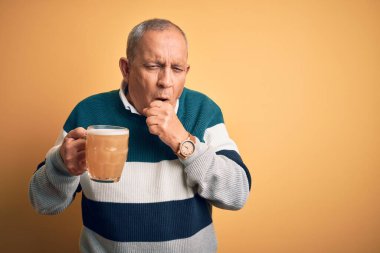 Üst düzey yakışıklı adam izole edilmiş sarı arka planda duran bira kavanozunu içiyor kendini iyi hissetmiyor ve soğuk algınlığı veya bronşitin belirtisi olarak öksürüyor. Sağlık hizmeti kavramı.