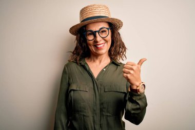 Orta yaşlı esmer kadın gözlüklü ve şapkalı. İzole edilmiş beyaz arka planda duruyor. Gülümsüyor, gülümsüyor..