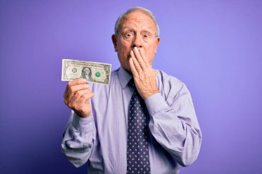 Kıdemli gri saçlı adam mor arka planda bir dolarlık banknot tutuyordu. Ağzı kapalıydı. Utancından ağzı açık kalmıştı.