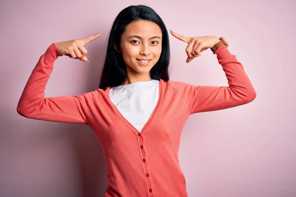 Young beautiful chinese woman wearing casual sweater over isolated pink background smiling pointing to head with both hands finger, great idea or thought, good memory