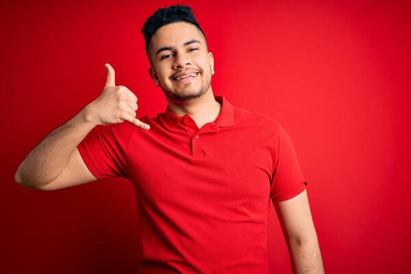 Young handsome man wearing red casual polo standing over isolated background smiling doing phone gesture with hand and fingers like talking on the telephone. Communicating concepts.