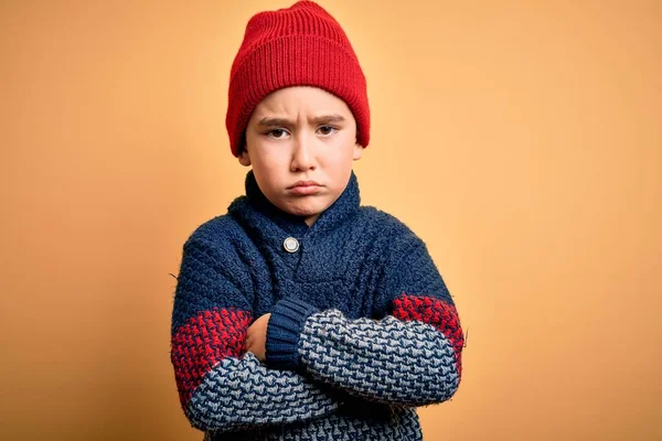 若い男の子のウールキャップと冬のセーターを身に着けている黄色の孤立した背景懐疑的で緊張し 両腕を組んで顔に不承認式 負の人 — ストック写真