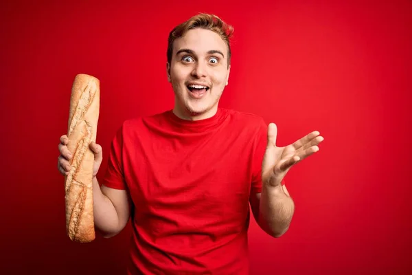 Young Handsome Redhead Man Holding Fresh Homemade Bread Isolated Red — Stock Photo, Image