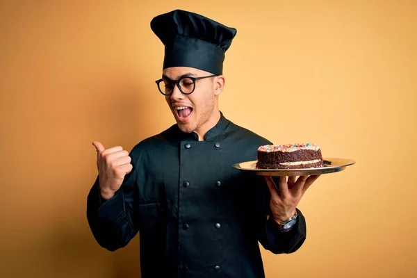 요리사 복장을 모자를 케이크를 가리키며 손가락을 옆으로 내밀고 미소를 제빵사 — 스톡 사진