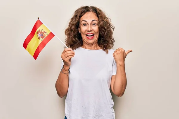 中年美丽的爱国妇女举着西班牙国旗 身披孤立的白色背景 大拇指指向侧面 嘴角张开 喜形于色 — 图库照片