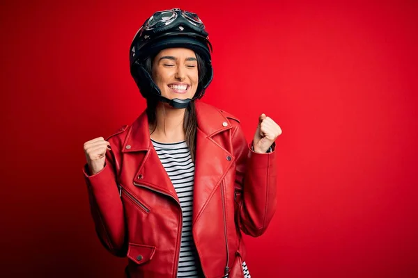 若い美しいブルネットのオートバイのヘルメットと赤いジャケットを身に着けているオートバイの女性は非常に幸せと腕を上げて勝者のジェスチャーを行う興奮し 笑顔と成功のために叫んでいます お祝いのコンセプト — ストック写真