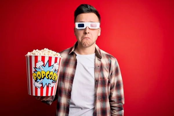 Young handsome caucasian man wearing 3d movie glasses and eating popcorn depressed and worry for distress, crying angry and afraid. Sad expression.