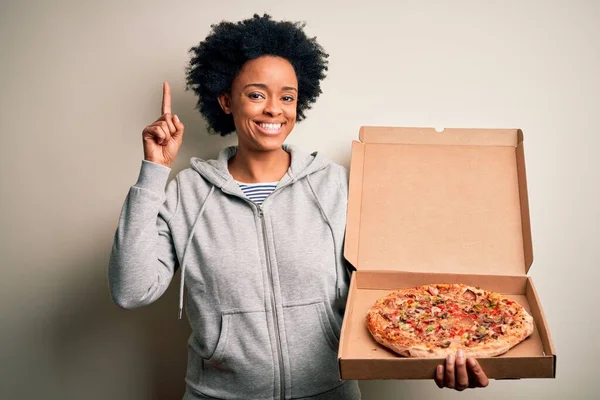 若いですアフリカ系アメリカ人アフロ女性とともに巻き毛保持配達ボックスでイタリアのピザ驚きでアイデアや質問を指差す指で幸せな顔 ナンバーワン — ストック写真