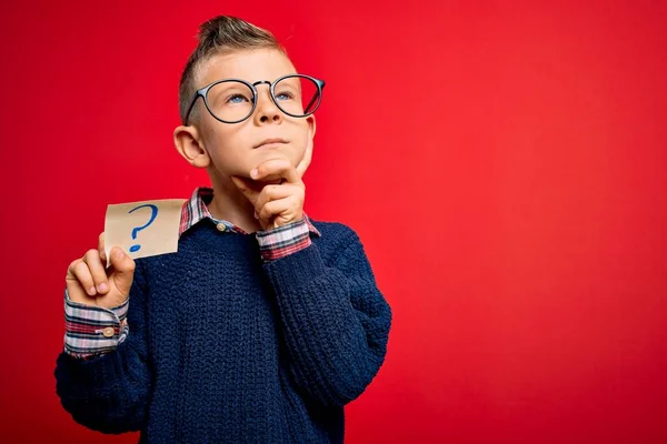年轻的白人小孩戴着眼镜拿着写有问号的纸条严肃地思考问题 非常迷惑的想法 — 图库照片