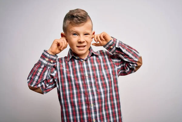 年轻的高加索小孩 蓝眼睛 穿着雅致的衬衫 站在孤立的背景上 用手指捂住耳朵 对嘈杂的音乐感到恼怒 聋人概念 — 图库照片