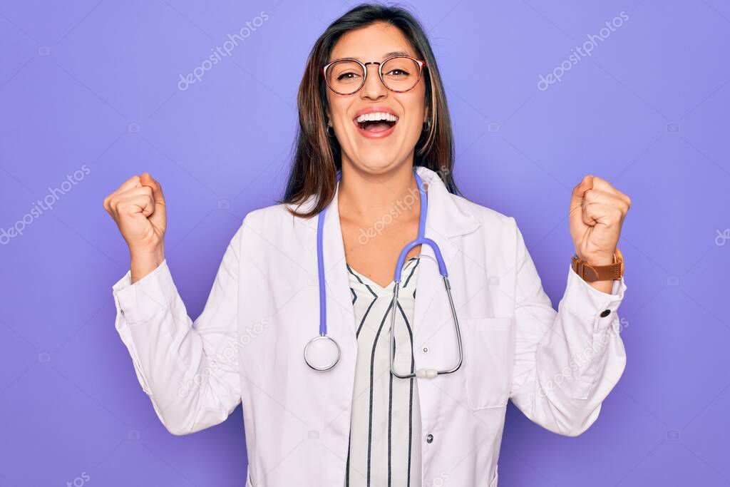 Professional doctor woman wearing stethoscope and medical coat over purple background celebrating surprised and amazed for success with arms raised and open eyes. Winner concept.