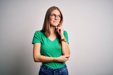 Genç, güzel, kızıl saçlı, sıradan yeşil tişörtler giyen ve beyaz arka planda gözlük takan, elleri çenesinde soru soran, düşünceli bir kadın. Gülen ve düşünceli bir yüz. Şüphe kavramı.
