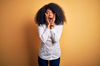 Afro saçlı, sarı arka planda duran güzel, Afro-Amerikan zarif genç bir kadın. Korkmuş ve şok olmuş, şaşırmış ve şaşırmış bir halde.