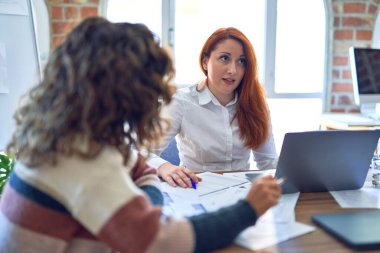 Birlikte çalışan mutlu ve kendinden emin gülümseyen iki güzel iş kadını. Ofiste gülümseyen bir gülümsemeyle oturuyor.