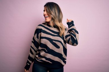 Moda kıyafetleri giyen genç ve güzel bir kadın. Manken, sokak tarzı giyiniyor. Pembe arka planda dikiliyor.