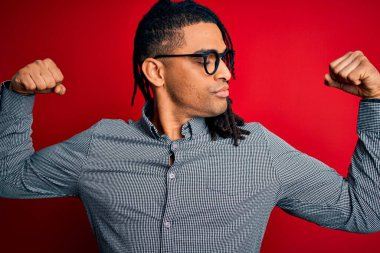 Rastgele gömlek ve gözlük takmış gururla gülümseyen kol kaslarını gösteren Afro-Amerikan genç adam. Fitness konsepti.